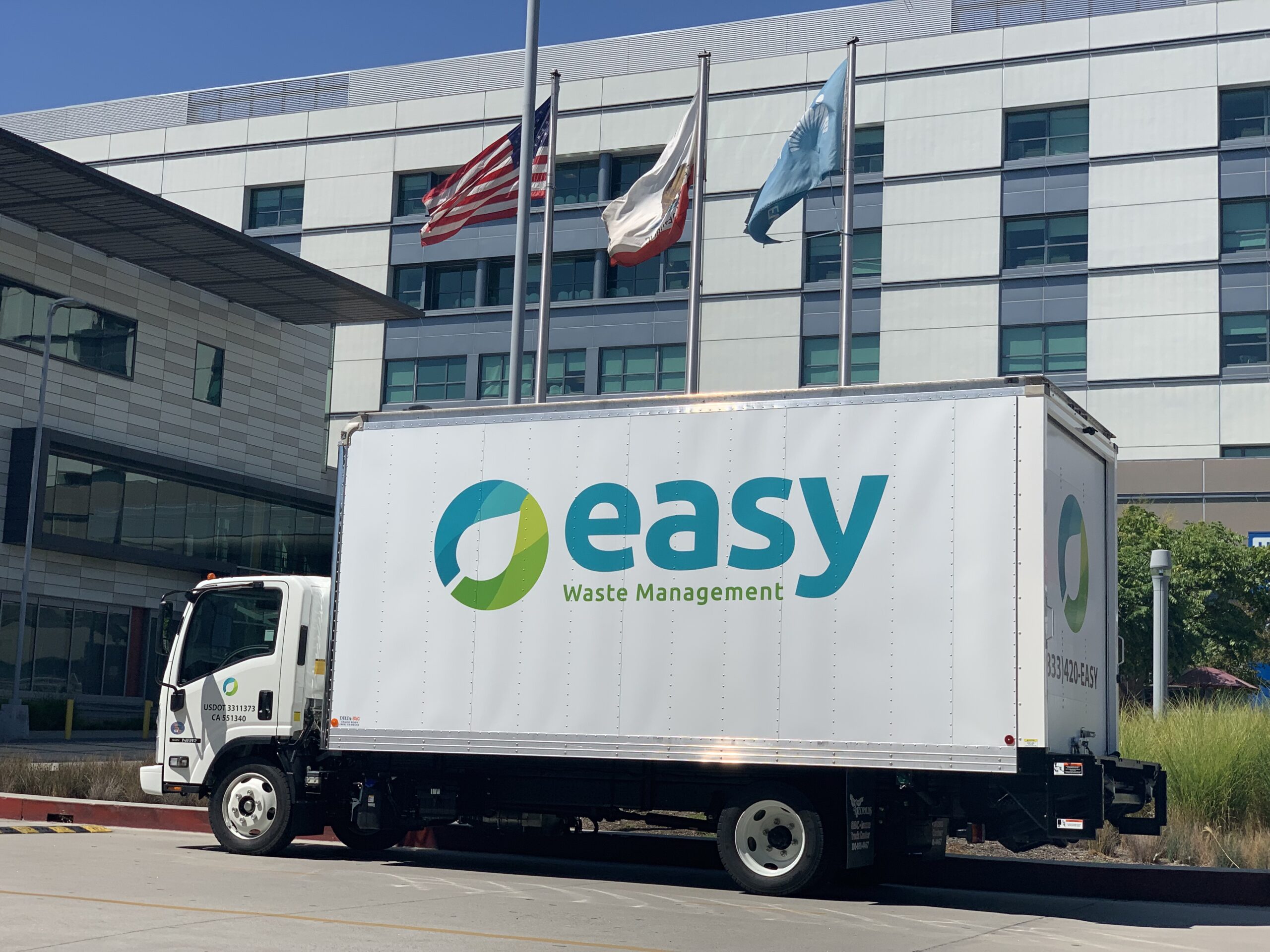 White truck with the "Easy Waste Management" logo parked in front of a building 